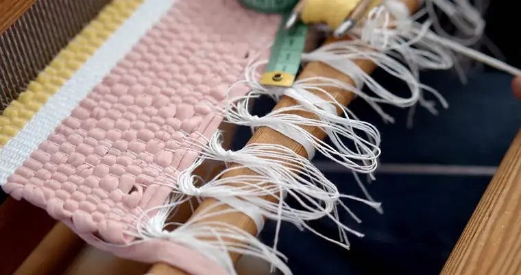 Franges en cours de nouage sur un tapis clair maintenu par une barre de tension