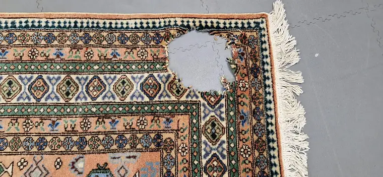 Coin d'un tapis d'Orient avec une large zone de velours arrachée avant restauration