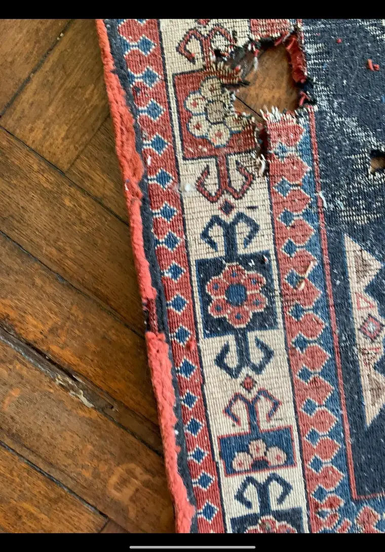 Trou et lisière rompue sur le bord d'un tapis ancien posé sur un parquet